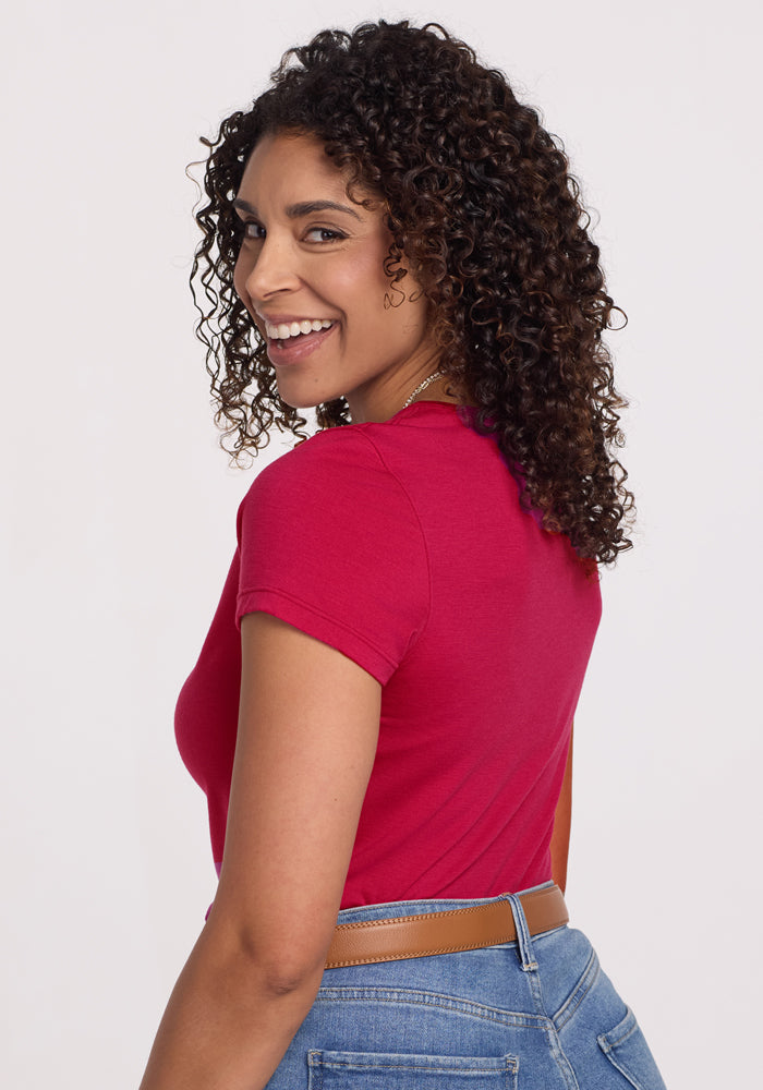 A woman with curly hair smiles over her shoulder in the Woolx Addie Crew Neck • Final Sale - Poppy Spark tee.