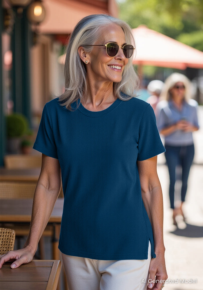Smiling older woman in sunglasses wears the Woolx Delia Ribbed Short Sleeve in Moroccan Blue by an outdoor café table.