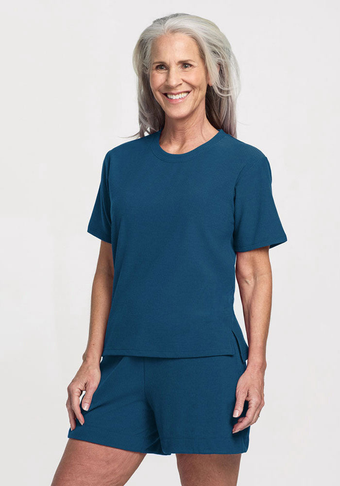 Smiling older woman in Woolx Delia Ribbed Short Sleeve and shorts in Moroccan Blue, standing against a plain background.