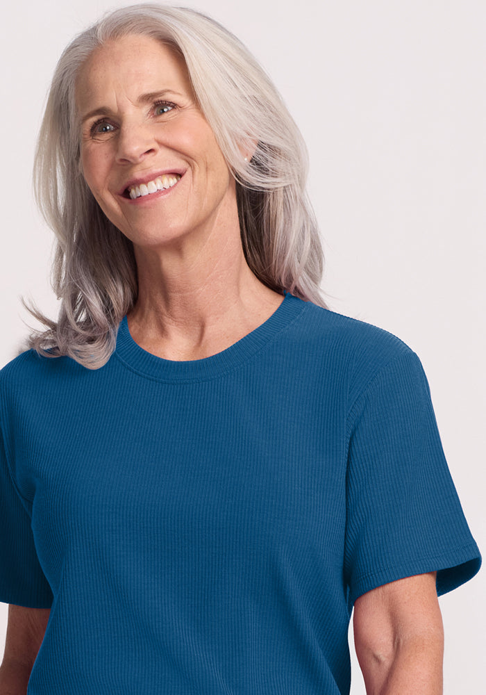 Smiling older woman in the Woolx Delia Ribbed Short Sleeve in Moroccan Blue, standing against a light background.