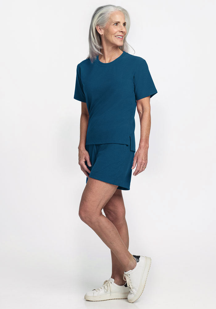Older woman wearing Woolx Delia Ribbed Short Sleeve in Moroccan Blue, smiling against a plain white background.