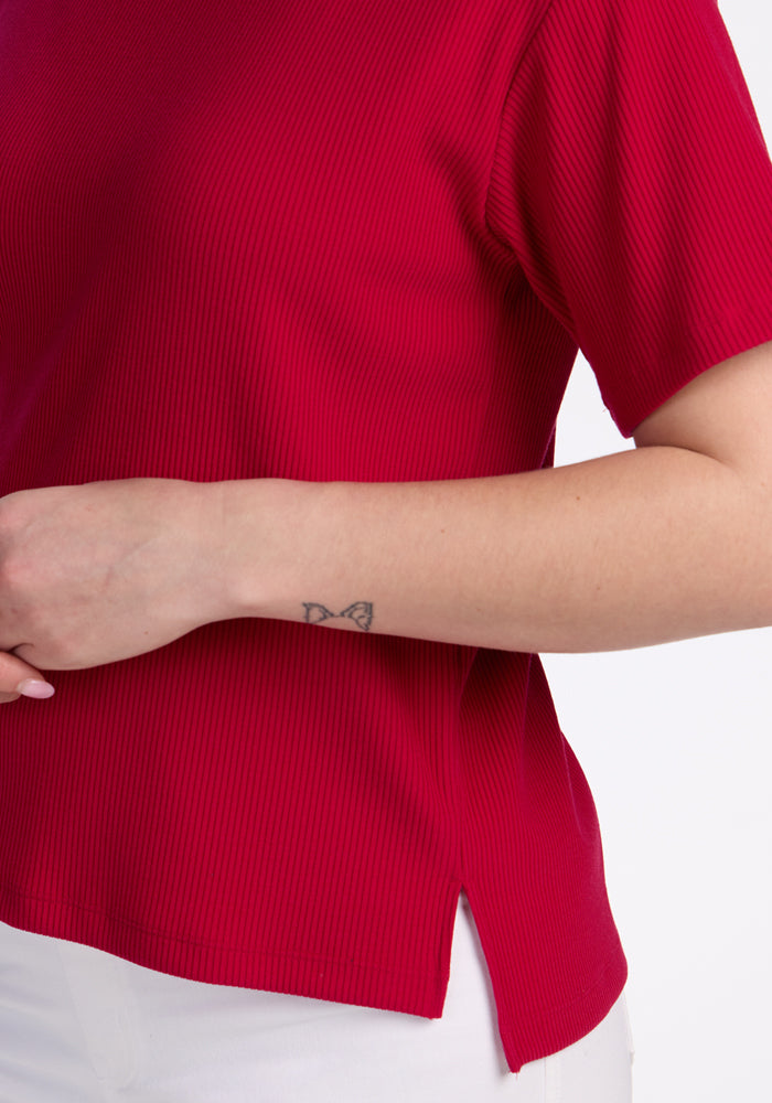 Wearing the Woolx Delia Ribbed Short Sleeve in Poppy Spark with white pants, showcasing a butterfly arm tattoo.