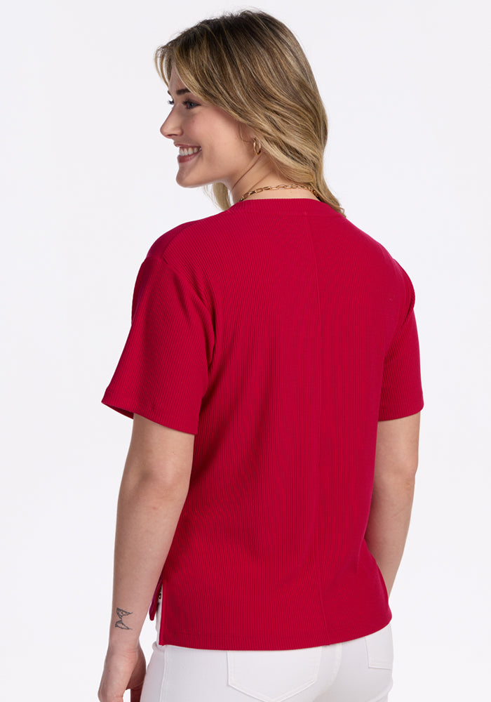 Woman smiles, facing away in Woolx Delia Ribbed Short Sleeve – Poppy Spark, with white pants on a white background.