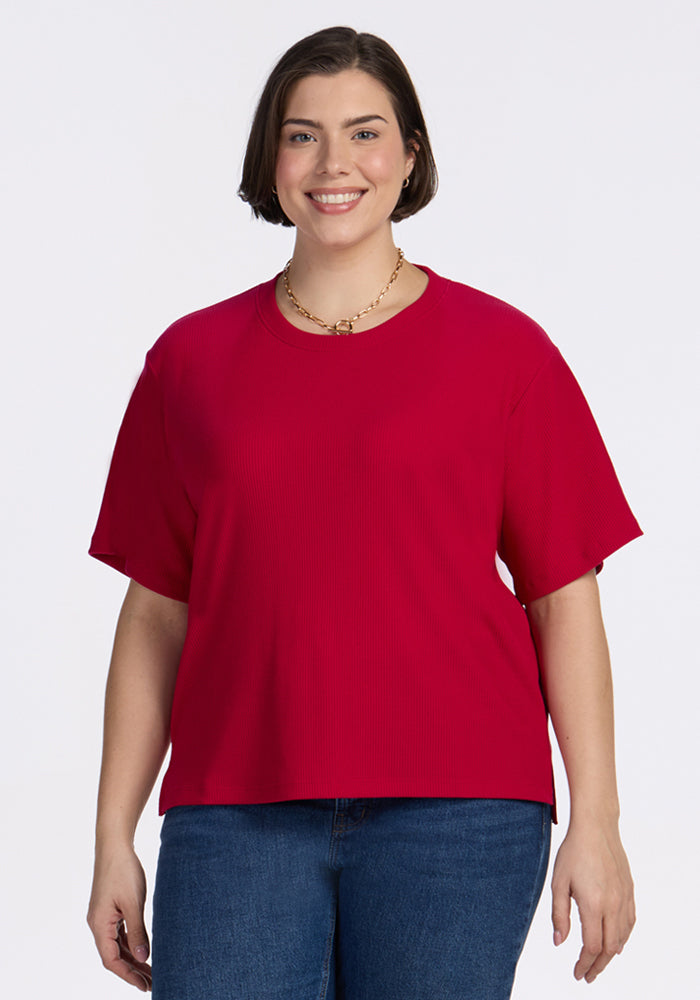 Smiling woman in the Woolx Delia Ribbed Short Sleeve in Poppy Spark, blue jeans, and gold necklace on white background.