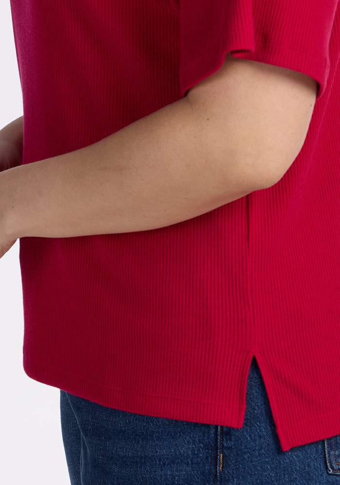 A person wears the Woolx Delia Ribbed Short Sleeve in Poppy Spark, paired with blue jeans.