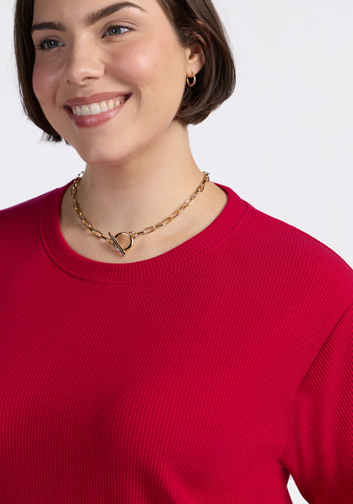 Woman smiles in the Woolx Delia Ribbed Short Sleeve in Poppy Spark, gold chain necklace, and small hoop earrings.
