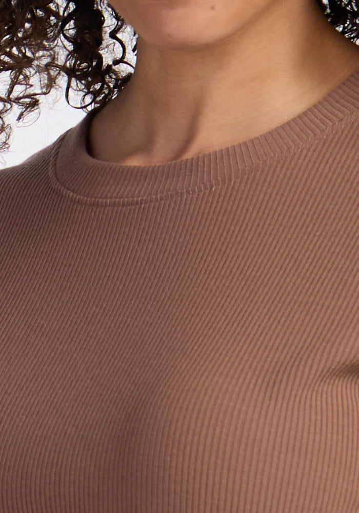 Close-up of a person in the Woolx Delia Ribbed Short Sleeve - Sienna Kiss, with curly hair partially visible.