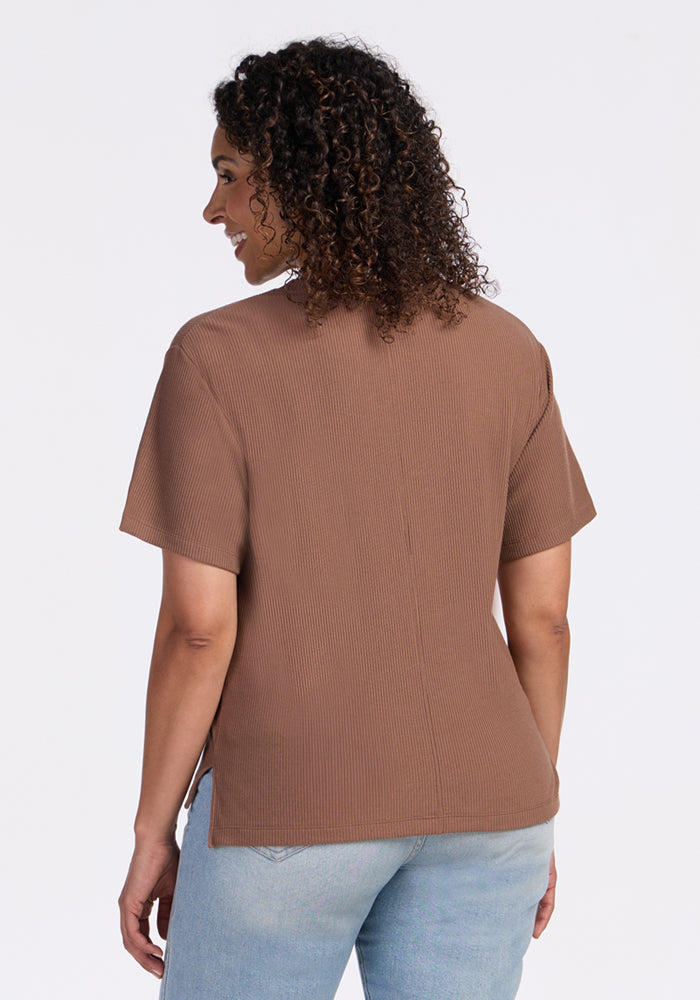 A woman with curly hair wears a Woolx Delia Ribbed Short Sleeve in Sienna Kiss and light blue jeans, back to camera.