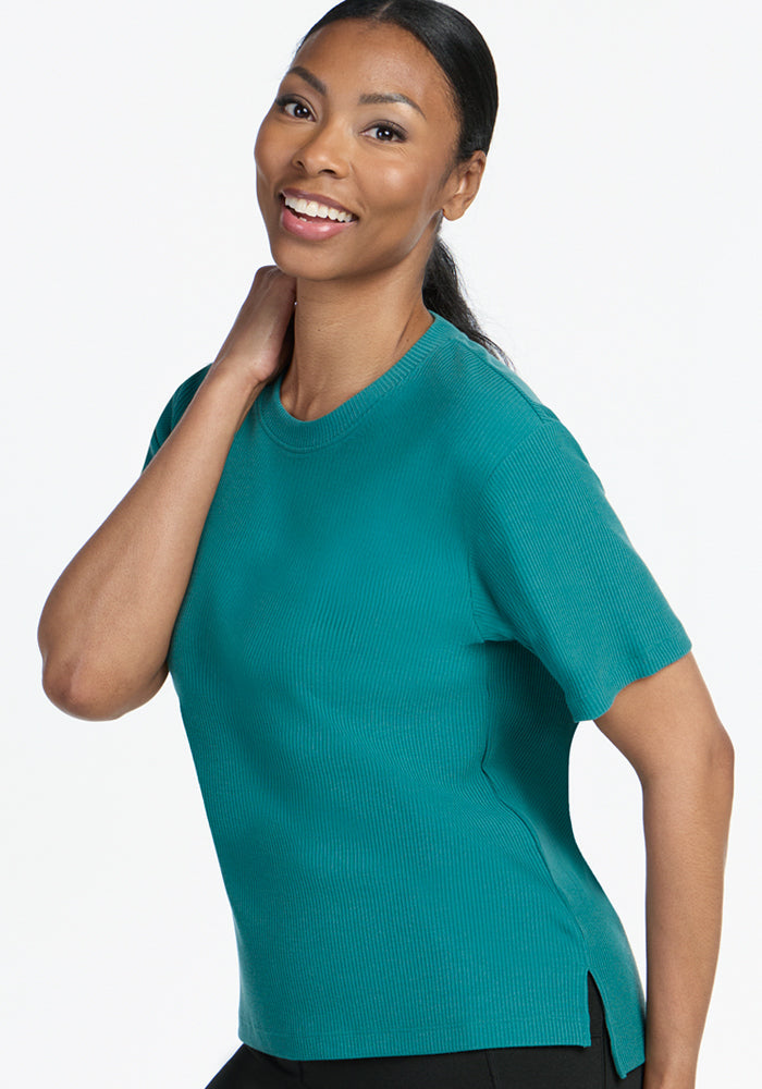 Smiling woman wears the Woolx Delia Ribbed Short Sleeve in Surfside, posing with a hand behind her neck.
