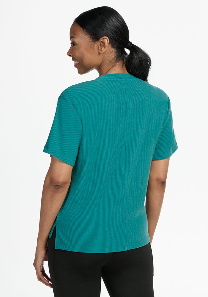 Woman in Woolx Delia Ribbed Short Sleeve - Surfside, shown from the back, smiling in black pants on white background.