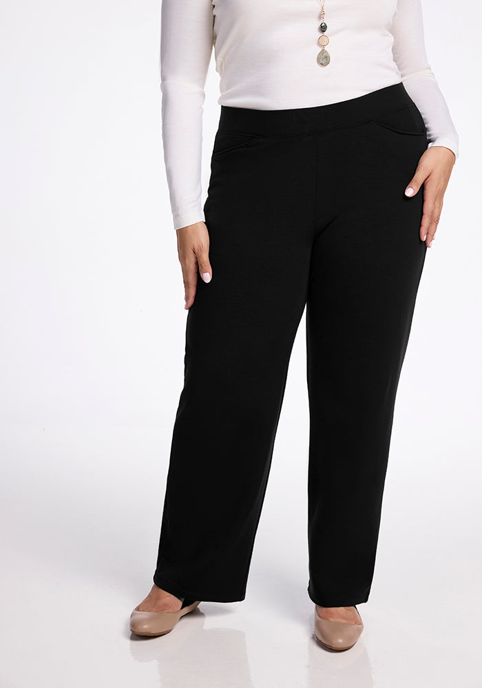 A person wearing a long-sleeve white top, Woolx Ellie Wide Leg Pants in black, and beige shoes stands against a white background. They are accessorized with a long necklace.