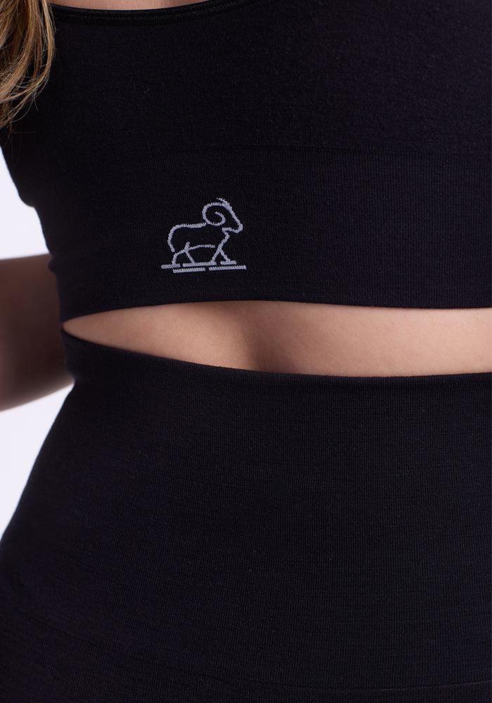 Close-up of a person wearing Woolx Ellis Seamless Tights in black and a crop top with an embroidered ram outline, highlighting the torso and bare midriff.
