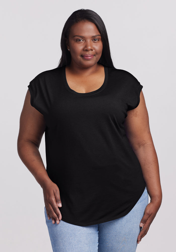 A woman with long black hair smiles, dressed in the versatile Gabi Tunic Top in black by Woolx and light blue jeans. She stands against a plain gray background, exuding effortless style. | Le'Quita is 5'11", wearing a size XL