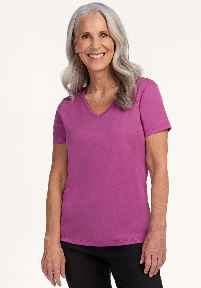 Smiling older woman in Woolx Junie V Neck in Purple Wine and black pants, with long gray hair.
