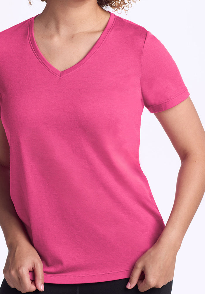 Woman wears the Woolx Junie V Neck in Raspberry Fizz, left hand near hip, against a plain background.