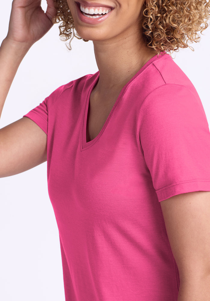 Smiling person with curly hair wearing the Woolx Junie V Neck in Raspberry Fizz against a light background.