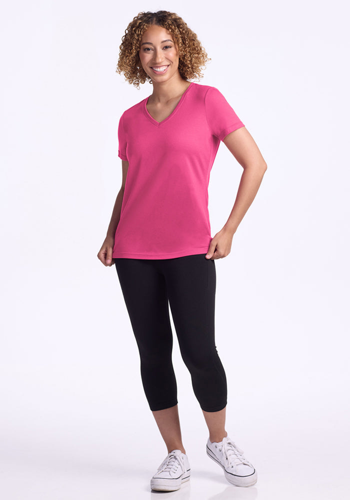 Woman smiling in a Woolx Junie V Neck in Raspberry Fizz with black leggings and white sneakers against a white background.