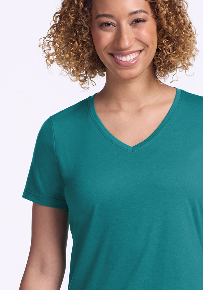 Smiling woman with curly hair wears the Woolx Junie V Neck in Surfside, waist up, against a light background.