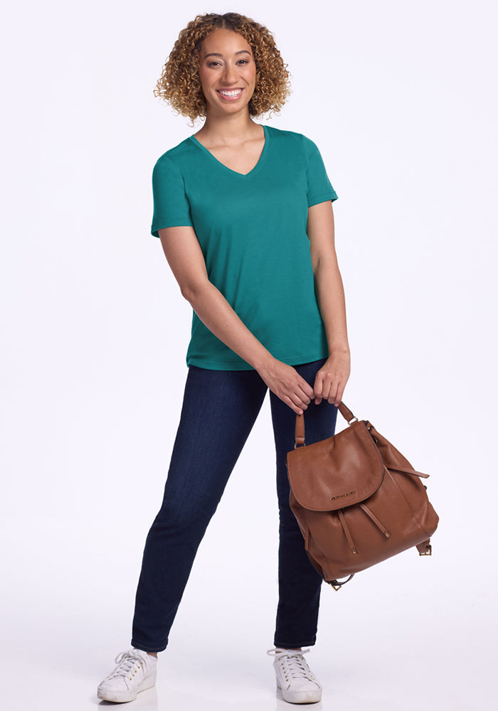 Woman in the Woolx Junie V Neck - Surfside, jeans, and white sneakers, smiling with a brown backpack.