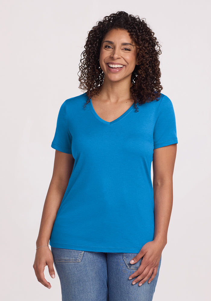 Smiling woman wears the Woolx Junie V Neck • Final Sale - Wave Rider tee with jeans against a plain light background.