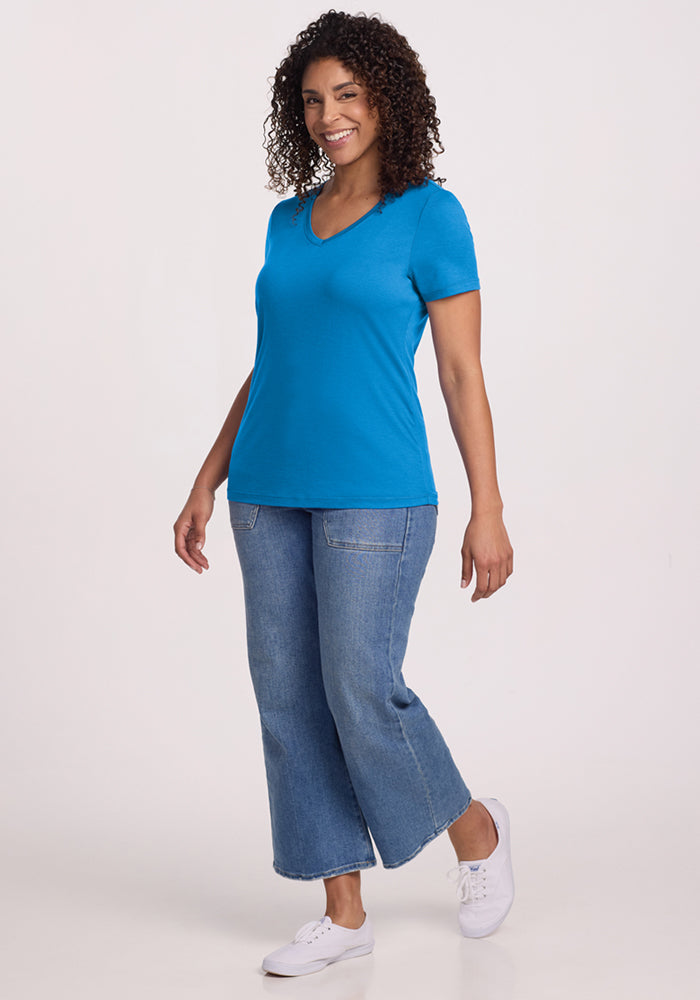 Woman smiling in the Woolx Junie V Neck tee in Wave Rider, cropped jeans, and white sneakers against a plain background.