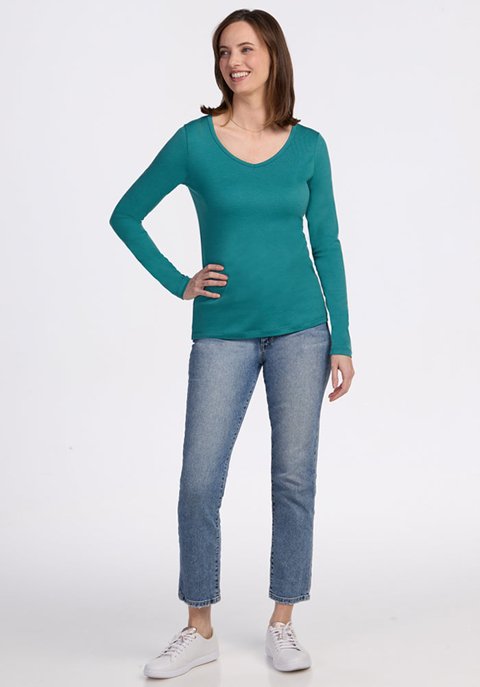 Woman smiling in a Woolx Layla V Neck Top in Surfside, blue jeans, and white sneakers.