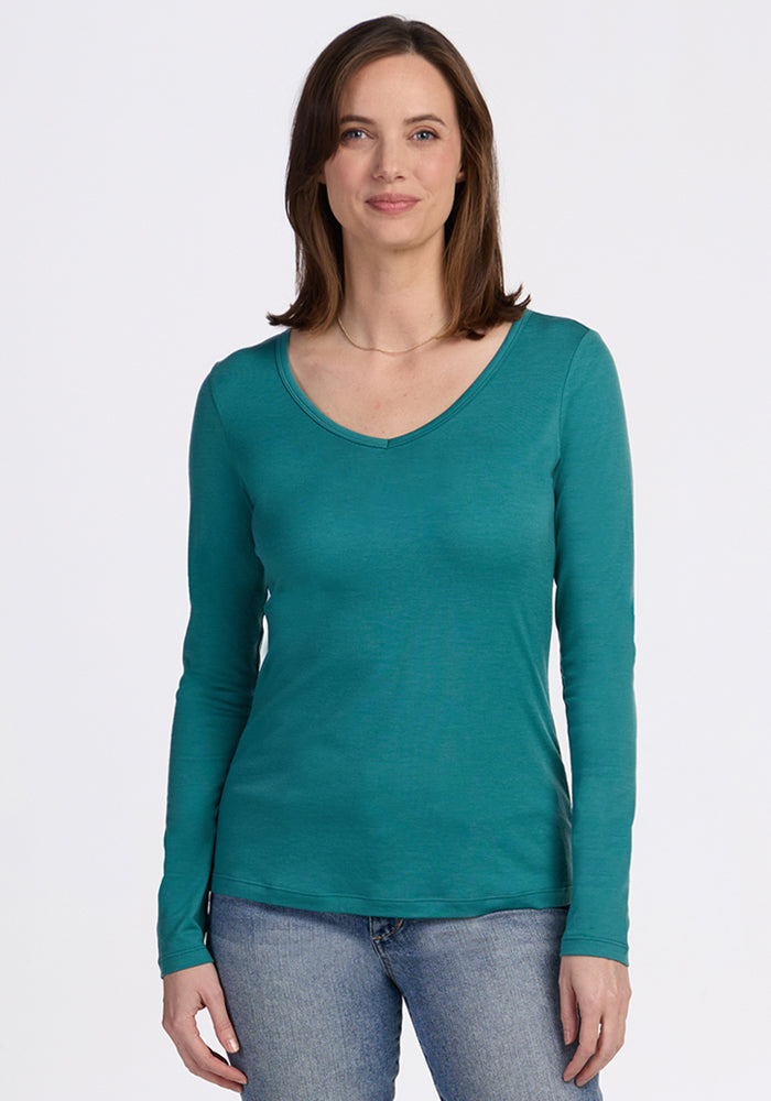 Woman wearing the Woolx Layla V Neck Top • Final Sale - Surfside and blue jeans, standing against a white background.