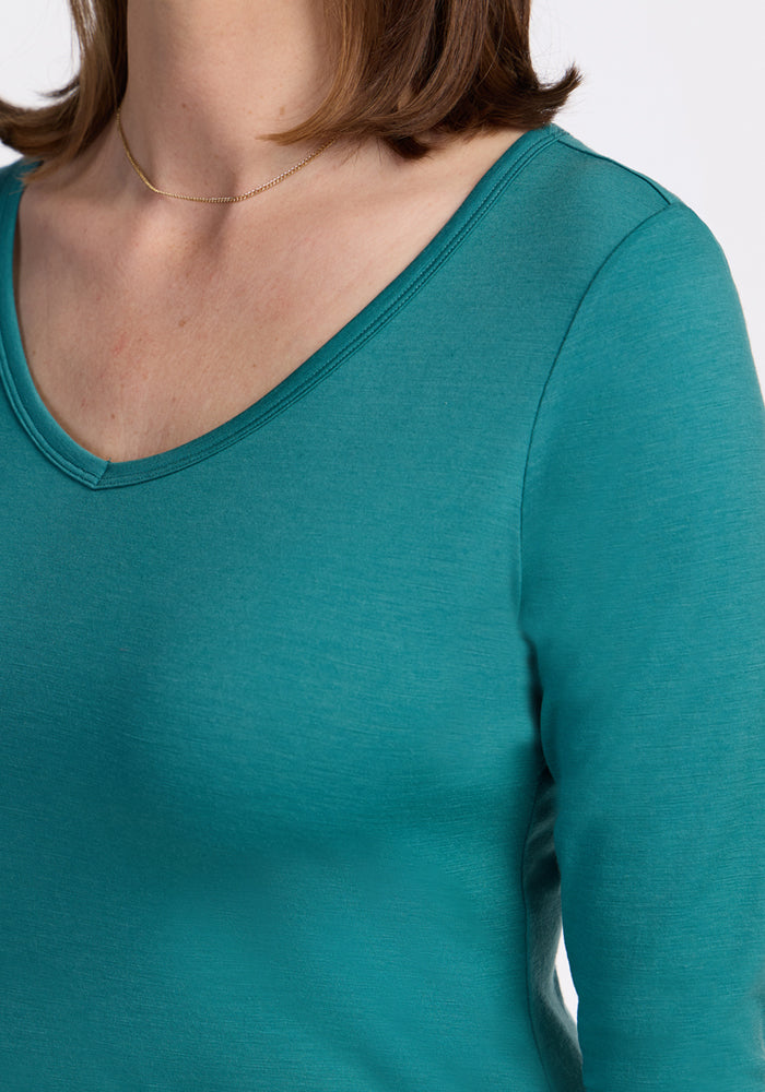 A person wears the Woolx Layla V Neck Top in Surfside and a thin gold necklace, shown from shoulders to upper chest.