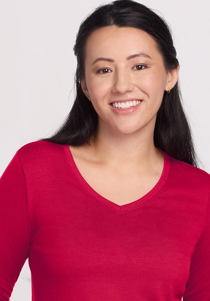 Smiling woman with long dark hair wears Woolx Millie Long Sleeve in Poppy Spark against a plain light background.