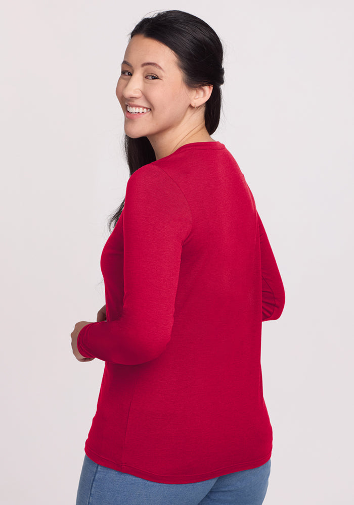 Woman with long dark hair in a Woolx Millie Long Sleeve - Poppy Spark top and jeans, smiling over her shoulder.