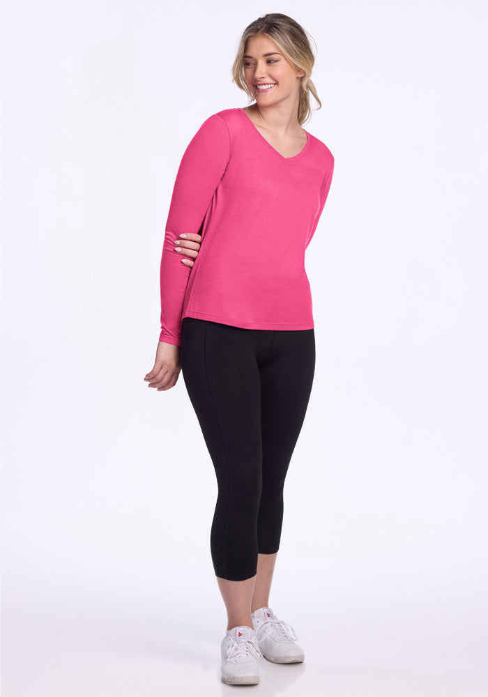 Woman wears Woolx Millie Long Sleeve in Raspberry Fizz, black capri leggings, and white sneakers, smiling.