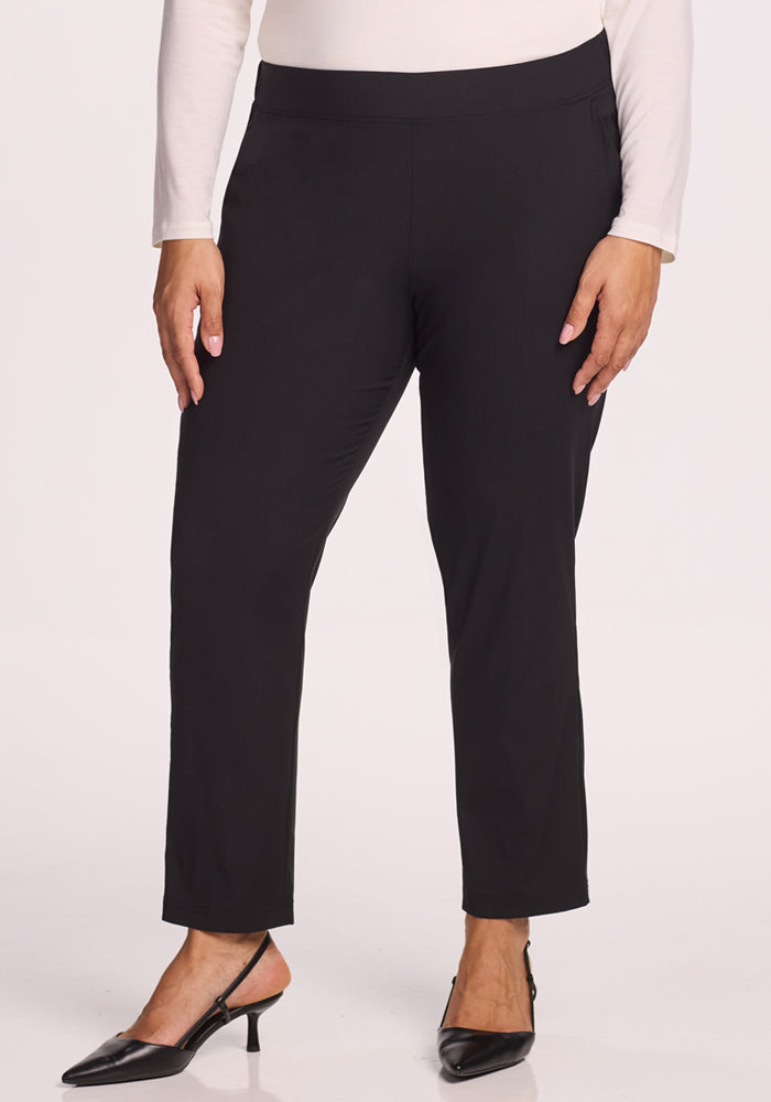 A person wearing Woolx Nicole Pants in black, paired with a long-sleeve off-white top and black pointed-toe heels, stands against a plain white background.