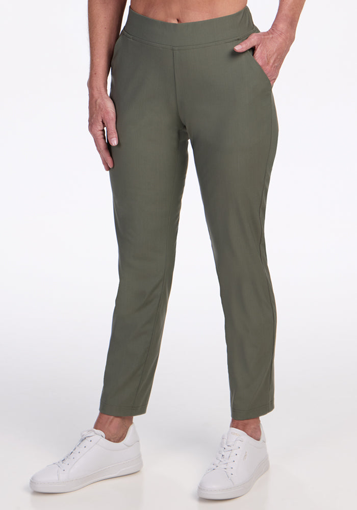 A person wearing Woolx Nicole Ankle Pants in Sage Olive and white sneakers stands with one hand in a pocket against a plain white background. | Tam is 5’8.5”, wearing a size S