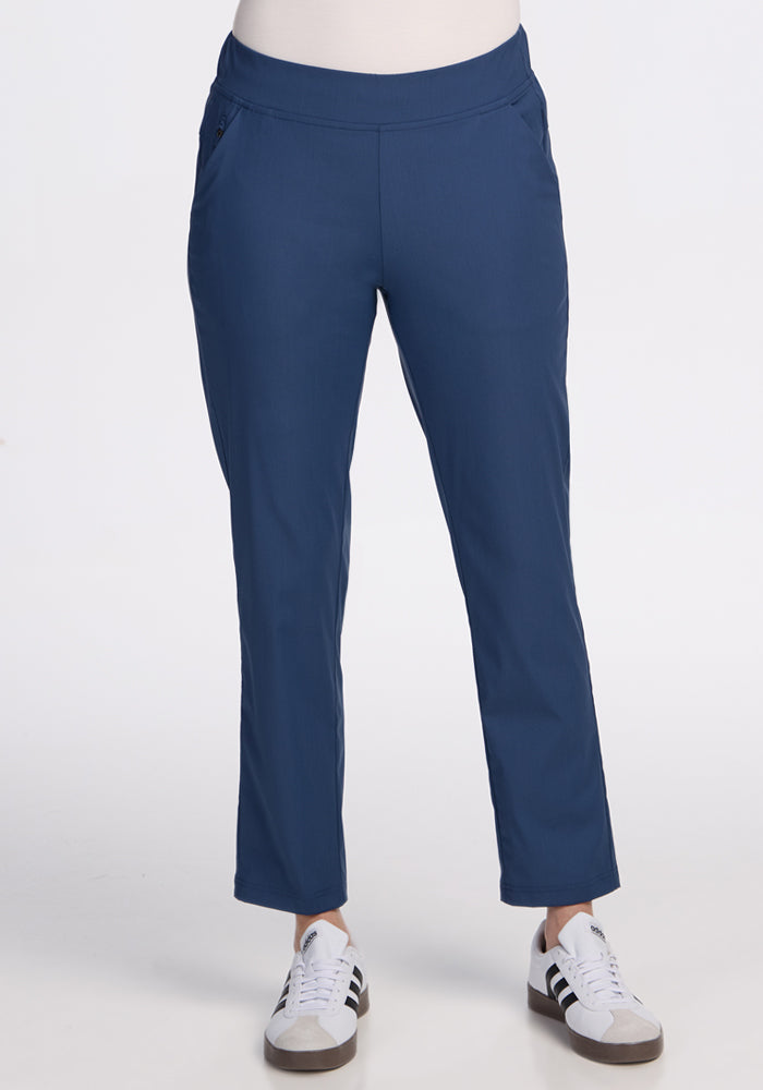 A person wearing Woolx Nicole Ankle Pants in Vintage Indigo pairs them with blue and white sneakers featuring black stripes, standing against a plain white background with hands in pockets. Only the lower half of their body is shown. | Jessica is 5’10”, wearing a size S