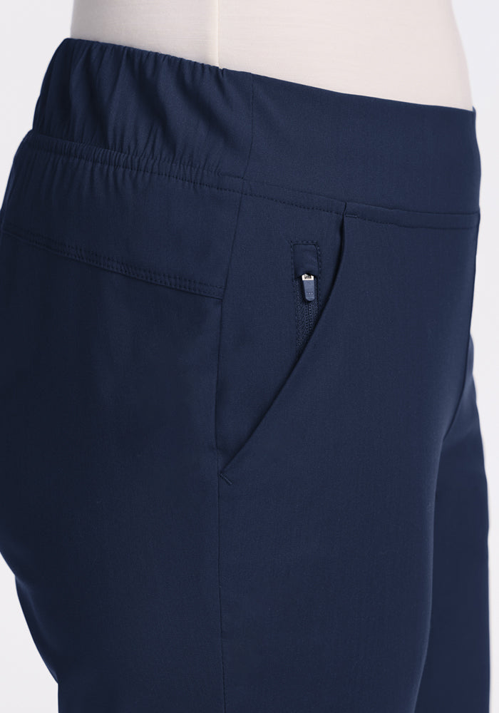 Close-up side view of a person wearing the Woolx Nicole Petite Ankle Pant in Deep Navy, featuring an elastic waistband and zippered pocket. The lightweight, tapered leg pants are set against a plain, light-colored background.