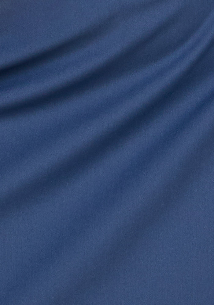 A close-up of smooth, soft blue fabric with flowing folds and subtle shadowing, echoing the refined texture of the Woolx Nicole Petite Ankle Pant in Vintage Indigo.
