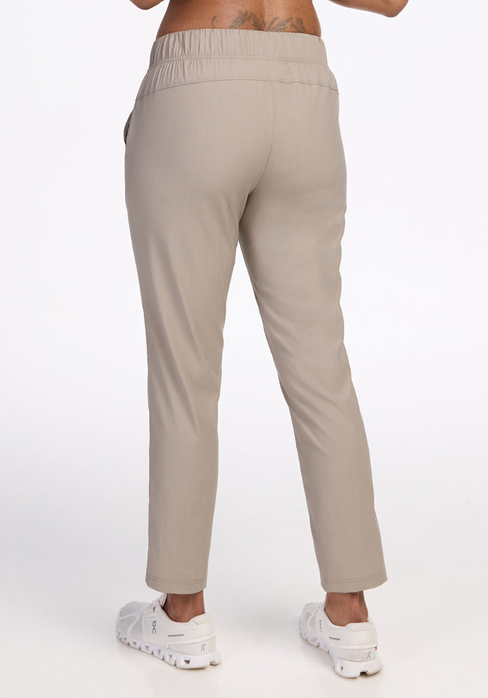 A person is shown from the back wearing Woolx’s Nicole Petite Ankle Pant in Vintage Khaki with a relaxed fit and elastic waistband, paired with white sneakers, standing against a plain white background.