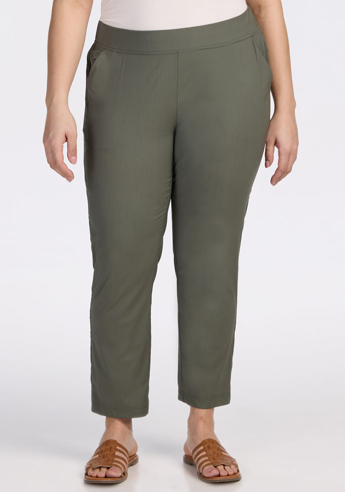 A person wears the Woolx Nicole Tall Ankle Pant in Sage Olive, paired with a white top and tan slide sandals, standing with arms relaxed at their sides against a plain white background.