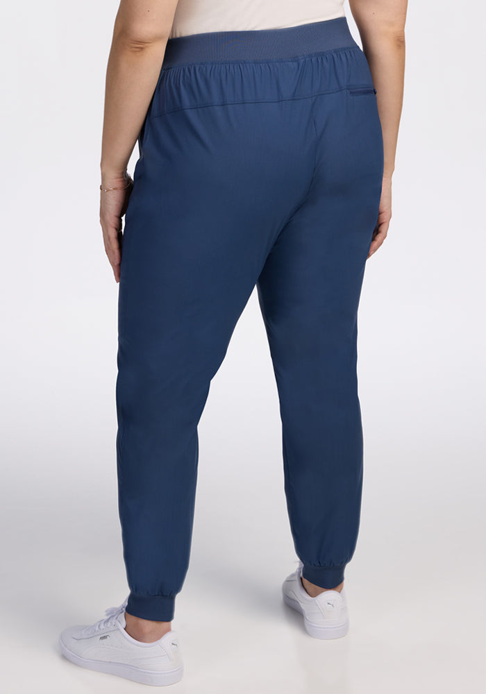 Someone is seen from behind against a plain white background, wearing Woolx Palmer Joggers in Vintage Indigo and white sneakers.