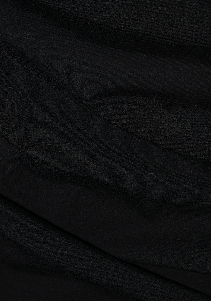 Close-up of the Piper Pocket Petite - Black fabric, by Woolx, showcasing subtle wavy folds that create a textured appearance. The material looks smooth and soft, similar to Merino wool leggings, with gentle shadows enhancing its draped look.
