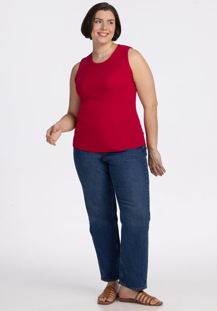 A woman with short brown hair smiles wearing the Woolx Raegan Ribbed Tank Top in Poppy Spark, blue jeans, and sandals.
