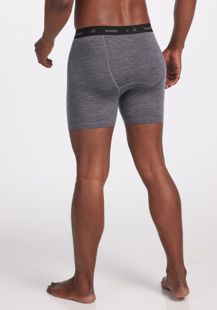 A person standing barefoot, facing away, wears Woolx Reaction Boxer Briefs in Graphite Heather with a black "woolx" waistband. Made from Merino Wool, these comfortable boxer briefs offer a sleek fit against the plain white background.