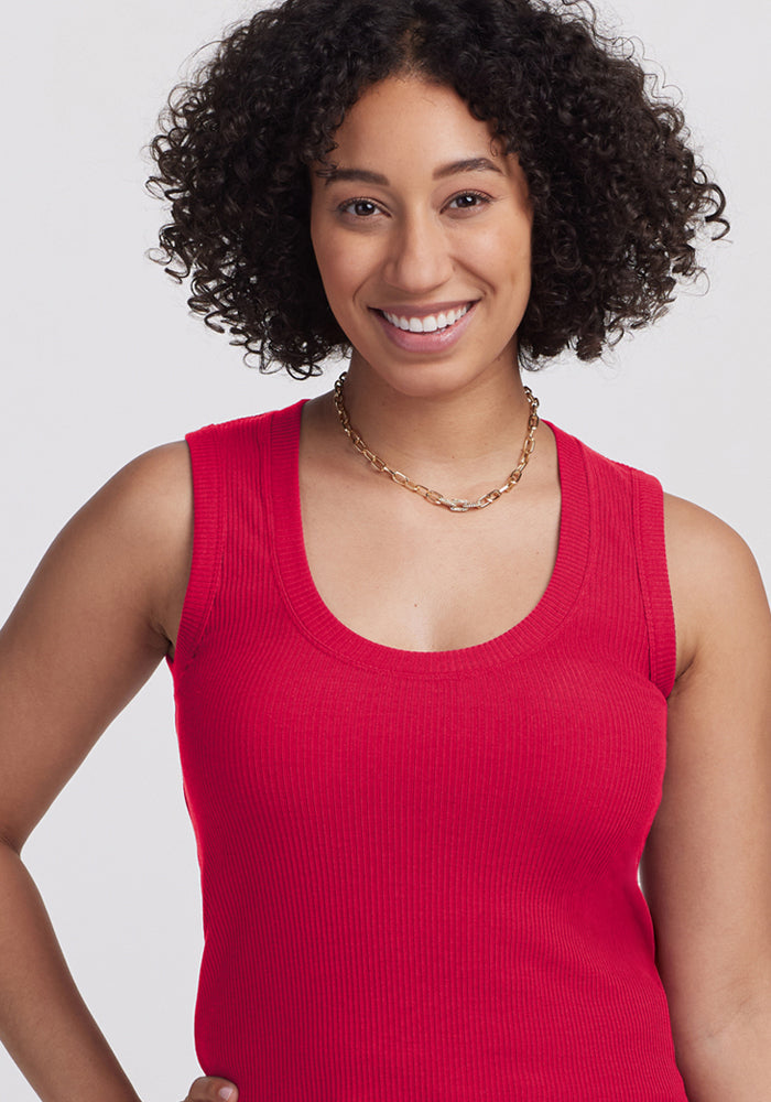 Smiling woman with curly hair wears the Woolx Sloane Ribbed Tank in Poppy Spark and a gold chain necklace.