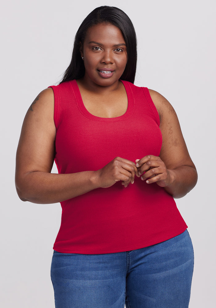 A woman wears the Woolx Sloane Ribbed Tank in Poppy Spark and blue jeans, standing against a light background.