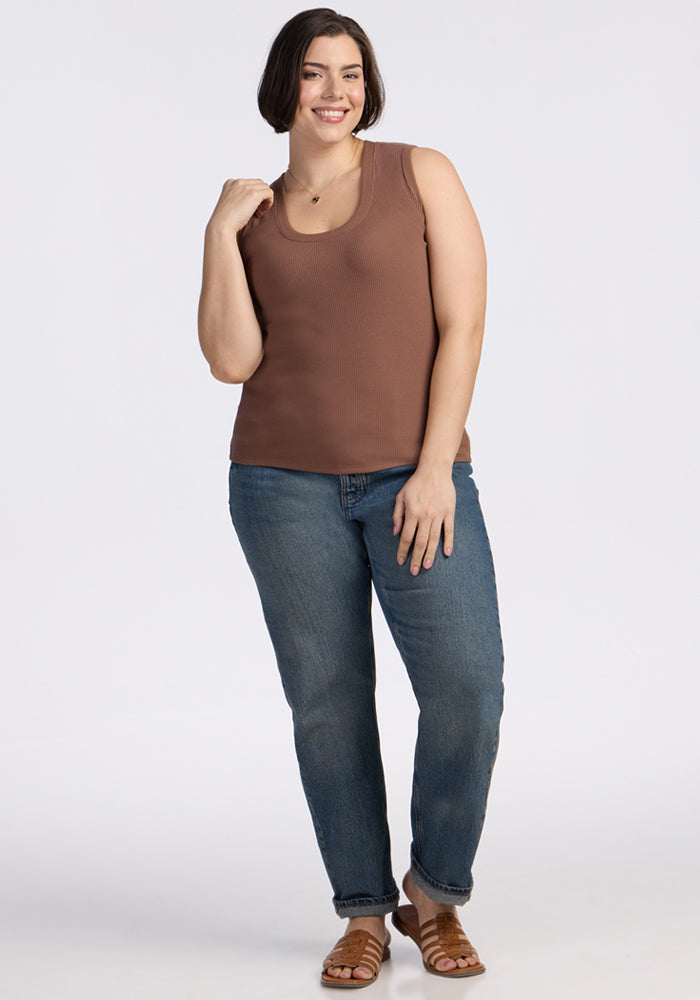 Smiling woman wears the Woolx Sloane Ribbed Tank in Sienna Kiss, blue jeans, and sandals against a white background.