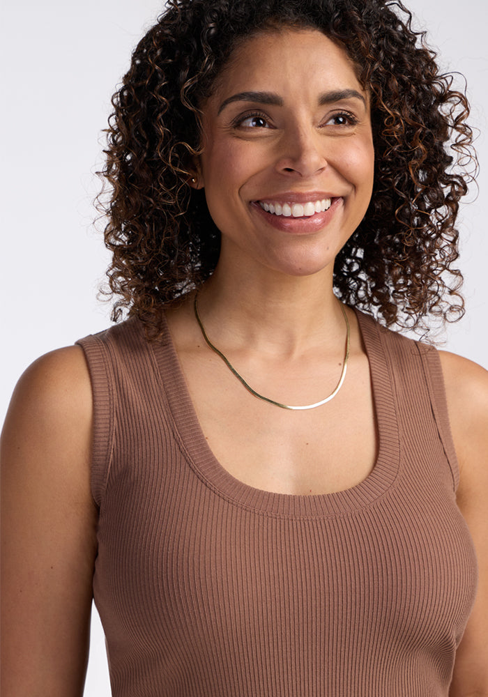 A smiling woman with curly hair wears the Woolx Sloane Ribbed Tank in Sienna Kiss and a simple gold necklace.