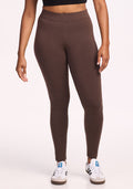 A person stands against a plain light background, wearing Woolx's Stella Petite merino wool leggings in Bracken and white sneakers with blue accents. The photo is cropped from the waist down.