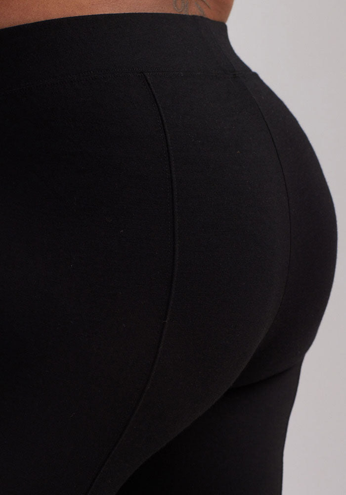 A close-up image of a person wearing Stella Tall - Black leggings from Woolx, highlighting the lower back and hip area. The fabric looks stretchy and form-fitting, providing comfort and flexibility. The background is a plain light color.