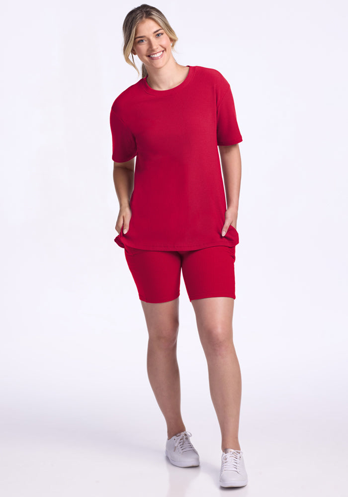 Woman smiles in Woolx Vera Ribbed Tunic • Final Sale - Poppy Spark, styled with white sneakers against a white background.