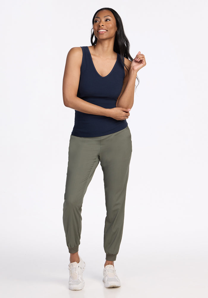 Woman wearing the Woolx Vivi Ribbed Tank in Deep Navy, olive joggers, and white sneakers smiles against a white background.